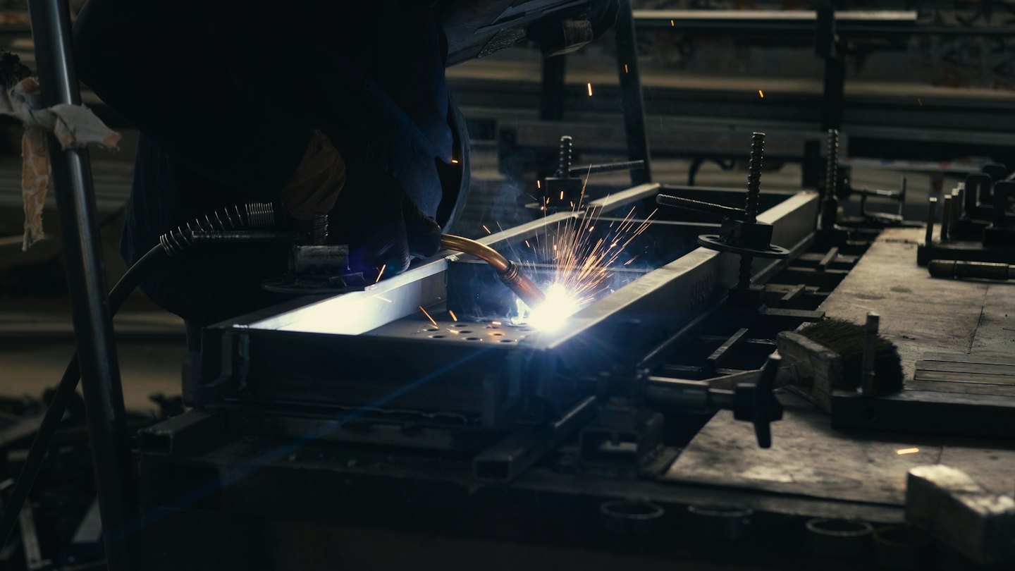 Worker welds metal in a workshop creating sparks.