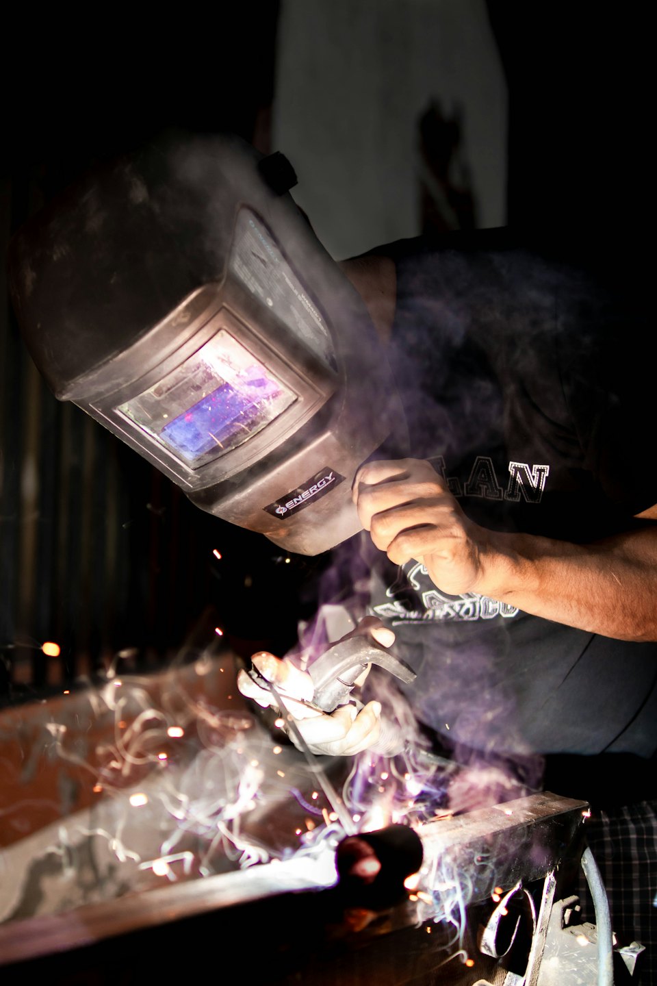 Welder in dark workshop sparks bright metal with welding gun.