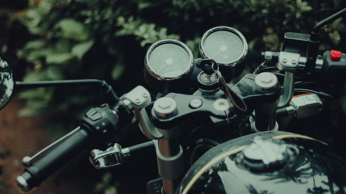 Motorcycle handlebars and dashboard parked in front of trees.