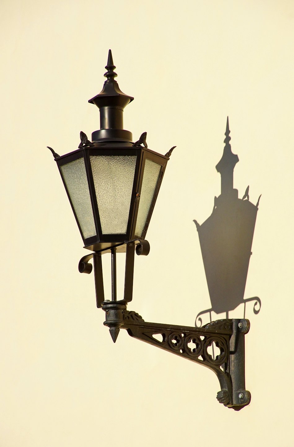 Ornate black metal lantern mounted on a smooth cream wall.