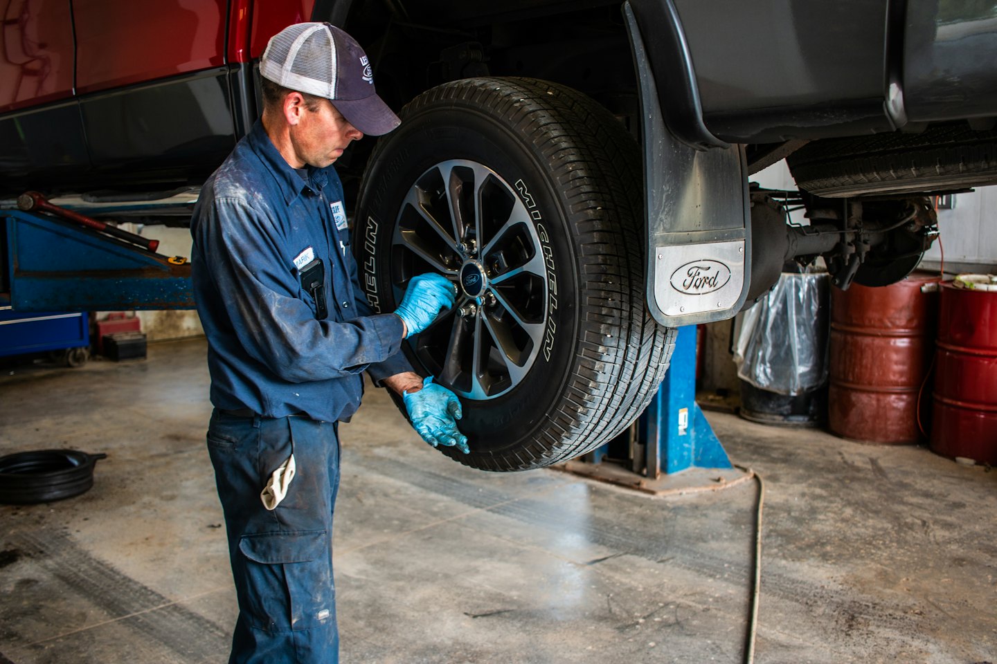 Mechanic in blue uniform fixing truck wheel on lift.